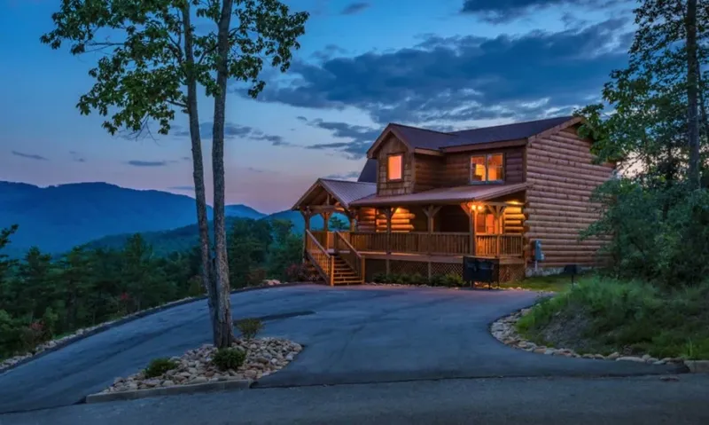 The cabin at dusk with the porch lights on and mountains behind